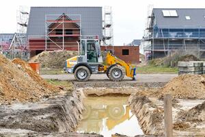 Bild vergrößern: Symbolbild Grundstückserschließung
Das Bild zeigt eine Baustelle in einem Neubaugebiet. In der Mitte des Bildes ist ein Bagger zu sehen. Hinter dem Bagger sind mehrer Häuser zu sehen.