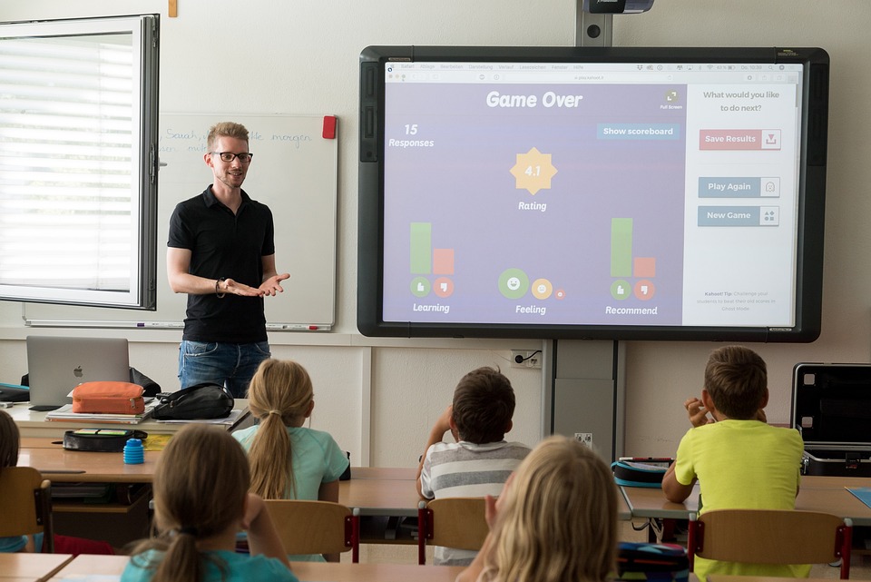 Das Bild zeigt einen Lehrer und Schüler in einem Klassenraum.