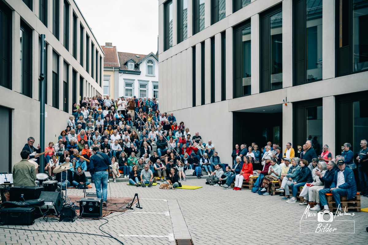 Das Bild zeigt die Zuschauermenge und die Band des letzten Treppenkonzerts zwischen den beiden Häusern des Rathauses.