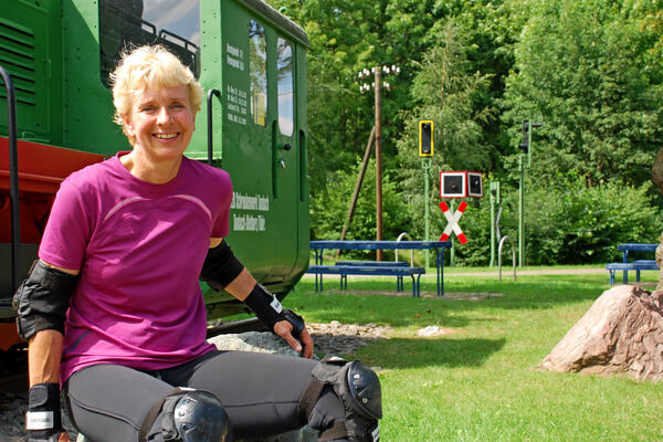 Bild vergrößern: Eine Frau sitzt am Radknoten Korbach auf einem Stein. Im Hintergrund ist die grüne Lok Emma zusehen.